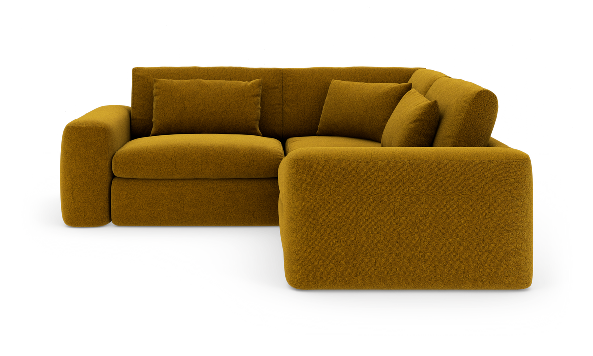 Sennepsgul hjørnesofa med bløde, afrundede former og tre puder, frilagt på hvid baggrund.