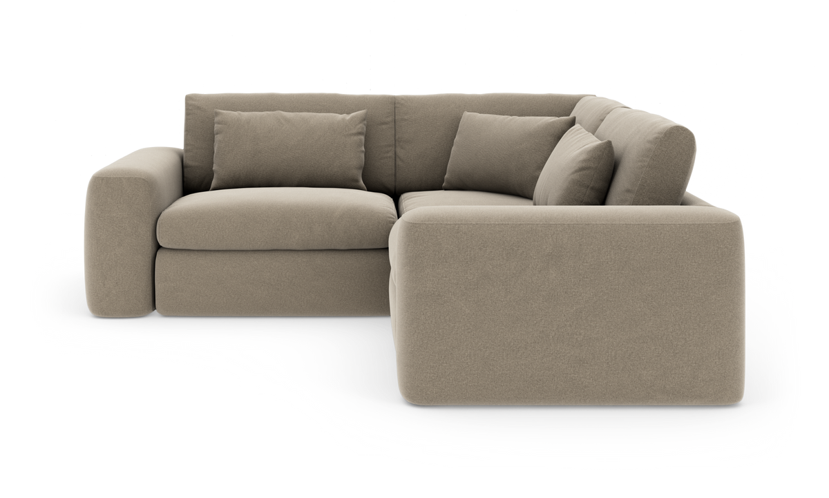 Beige hjørnesofa med bløde, afrundede former og tre ryghynder samt to pyntepuder, frilagt på hvid baggrund.