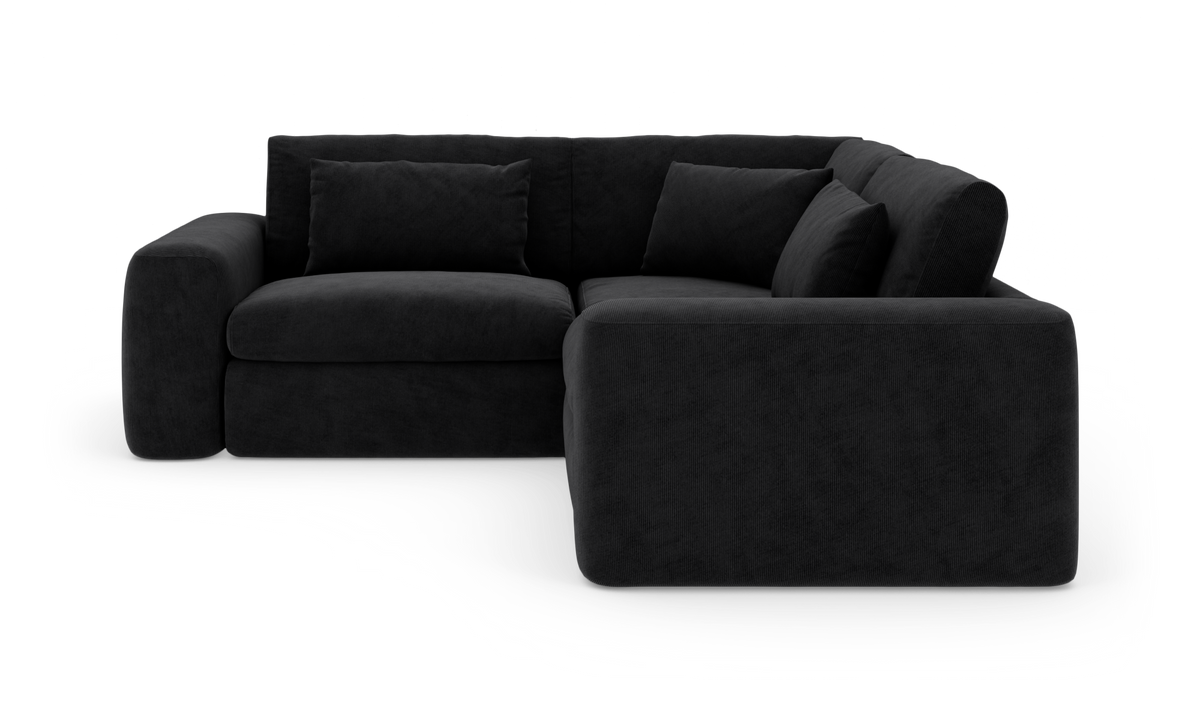 Sort modulær hjørnesofa med brede armlæn og løse ryghynder, fritlagt i studie.