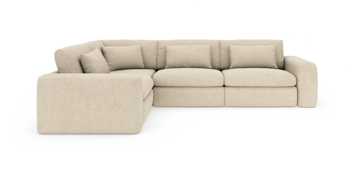 Beige modulsofa i L‑form med brede armlæn og løse ryghynder, frilagt på hvid baggrund.