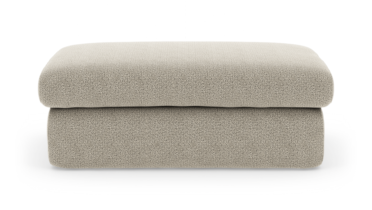 Beige rektangulær puf/ottoman i blødt boucléstof med afrundede kanter, frilagt på hvid baggrund.
