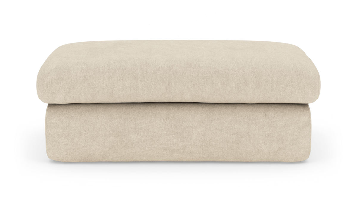 Beige rektangulær ottoman i stof på hvid baggrund.