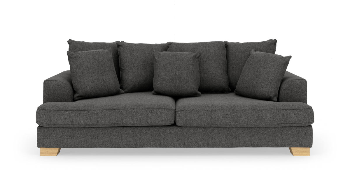 Mørkegrå sofa med flere løse puder og lyse træben, frontvisning.