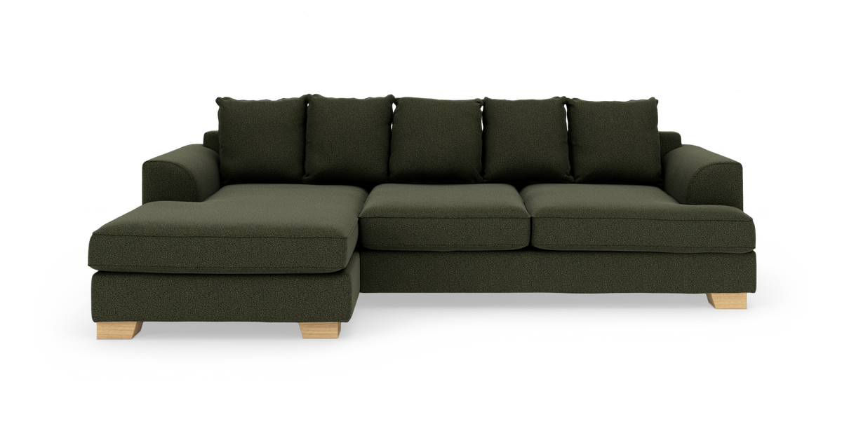 Mørkegrøn L‑sofa med venstrevendt chaiselong, løse rygpuder og lyse træben på hvid baggrund.