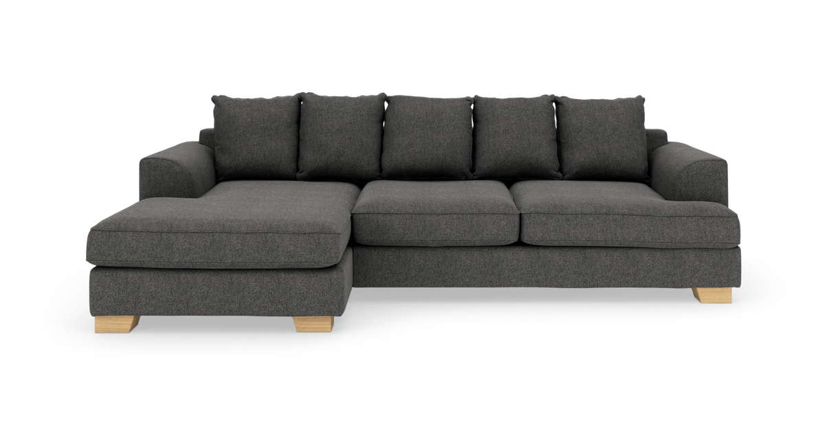 Mørkegrå hjørnesofa med venstrevendt chaiselong, løse ryghynder og lyse træben, frilagt på hvid baggrund.