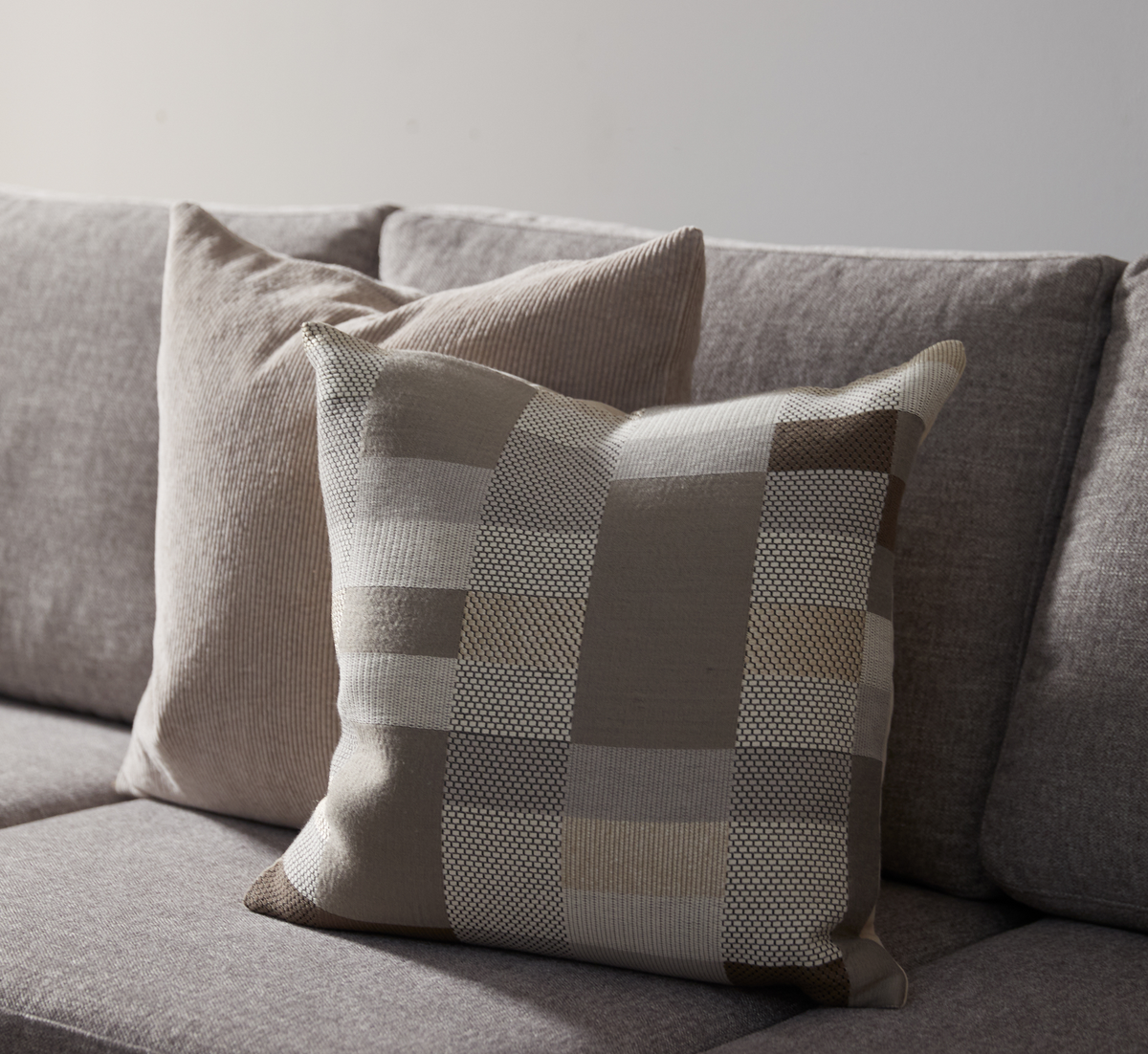 To pyntepuder i beige og grå nuancer på en grå sofa.