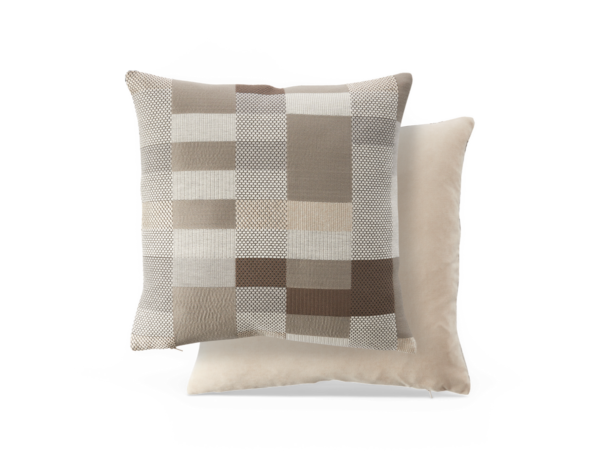To pyntepuder i neutrale toner, en med ternet patchwork i beige og brun foran en ensfarvet, velourlignende pude.