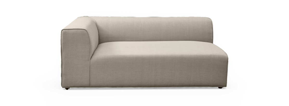 Beige modulsofa med ét armlæn, lav ryglæn og blødt afrundede kanter på sort baggrund.