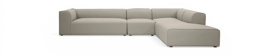 L-formet modulsofa i beige stof, frilagt på sort baggrund, set skråt forfra.