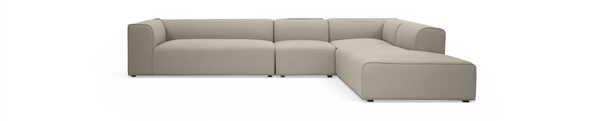 L-formet modulsofa i beige stof, frilagt på sort baggrund, set skråt forfra.