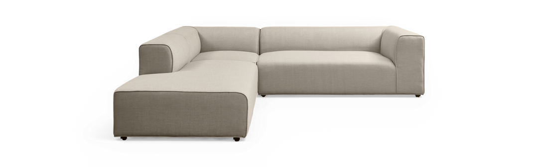 Beige L-formet modulsofa med venstrevendt chaiselong, afrundede hjørner og lav profil på sort baggrund.