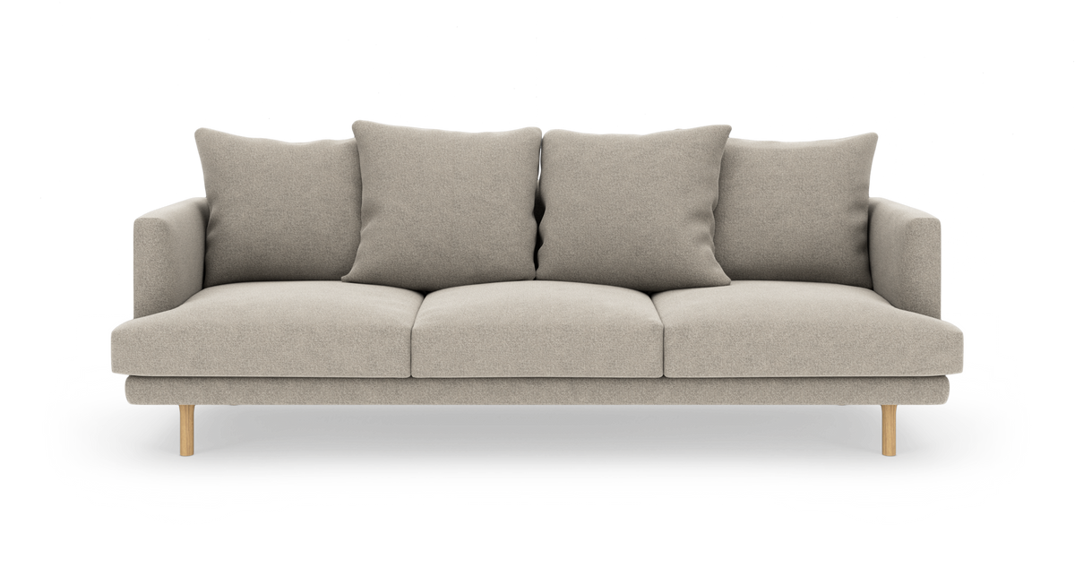 Beige 3-personers sofa med fire rygpuder og træben, frilagt på hvid baggrund.