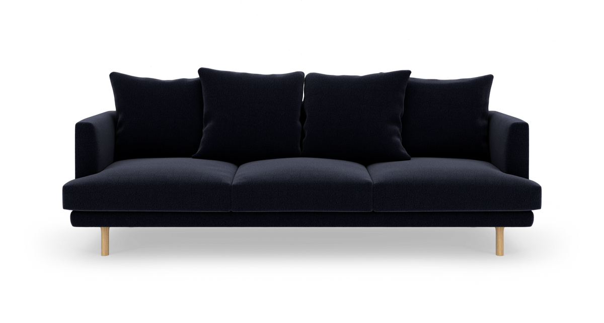 Mørkeblå 3‑personers sofa med fire store puder og lyse træben, frilagt mod hvid baggrund.