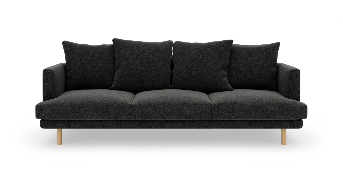 Sort tresædet sofa med fire store puder og lyse træben, frilagt på hvid baggrund.