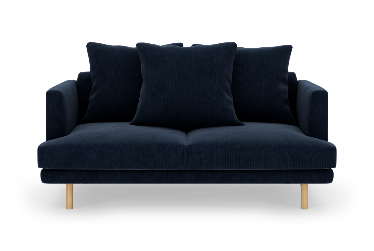 Mørkeblå sofa med tre store puder og lyse træben, fotograferet lige forfra.