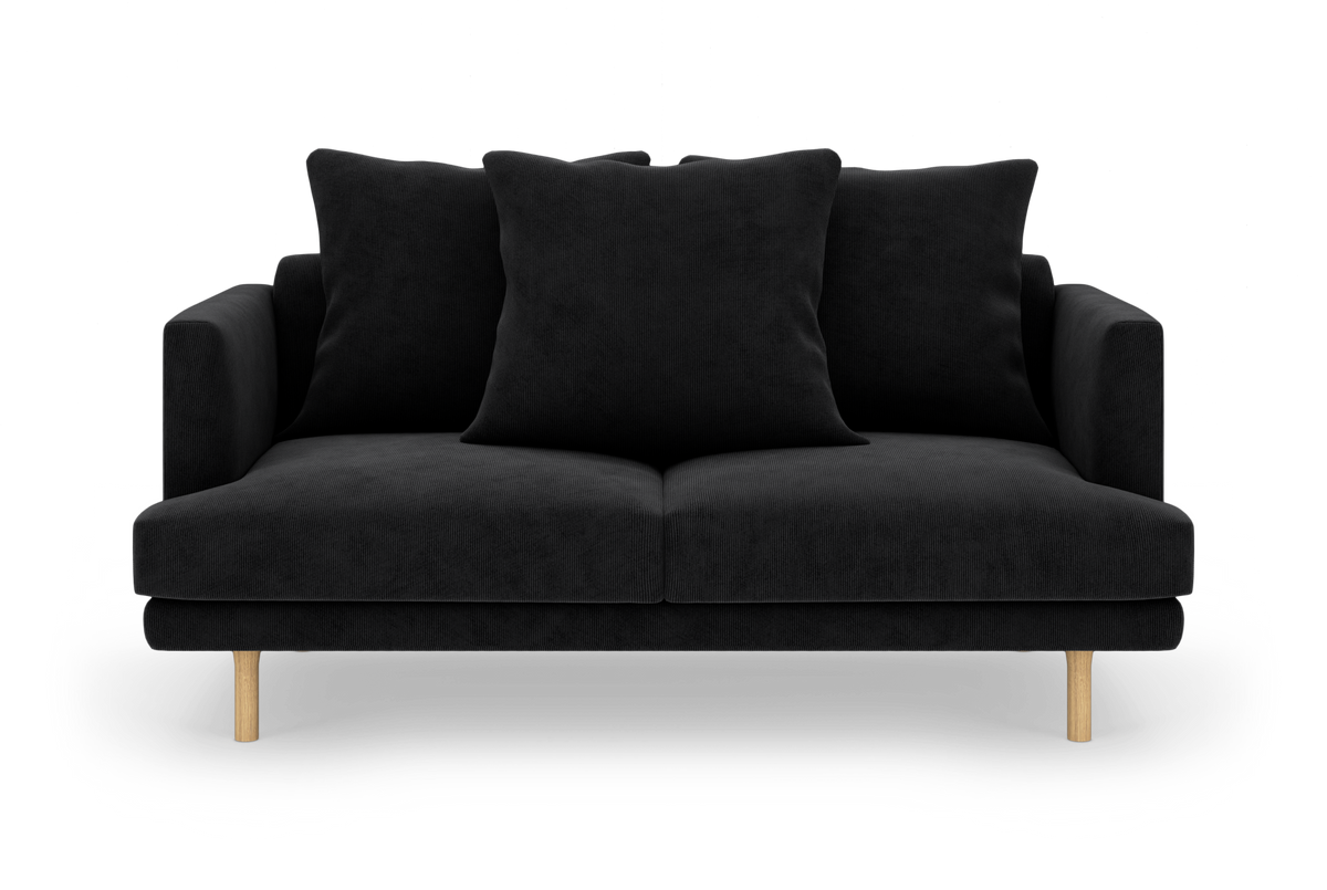 Sort 2-personers sofa med tre store puder og lyse træben, fotograferet lige forfra på hvid baggrund.