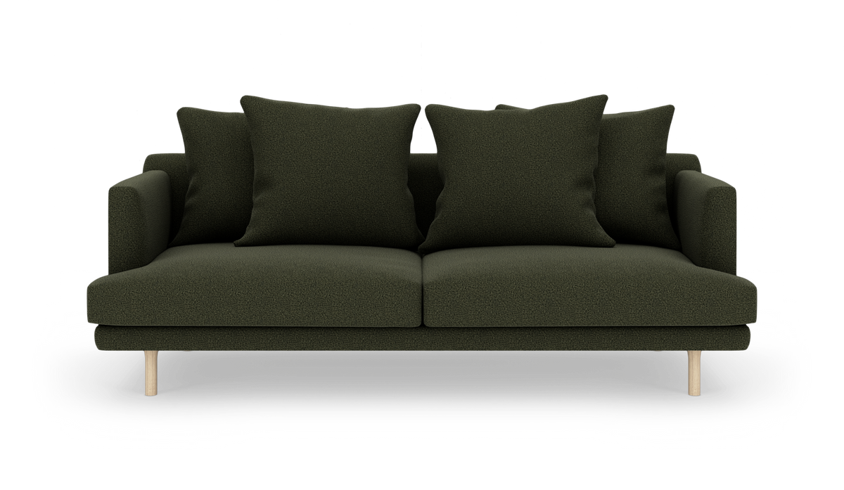 Mørkegrøn sofa med fire store puder og lyse træben, frilagt med skygge.