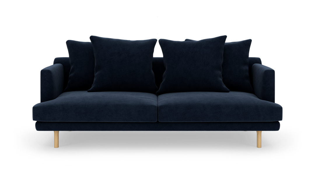 Mørkeblå sofa med fire store puder og lyse træben, frilagt på hvid baggrund.