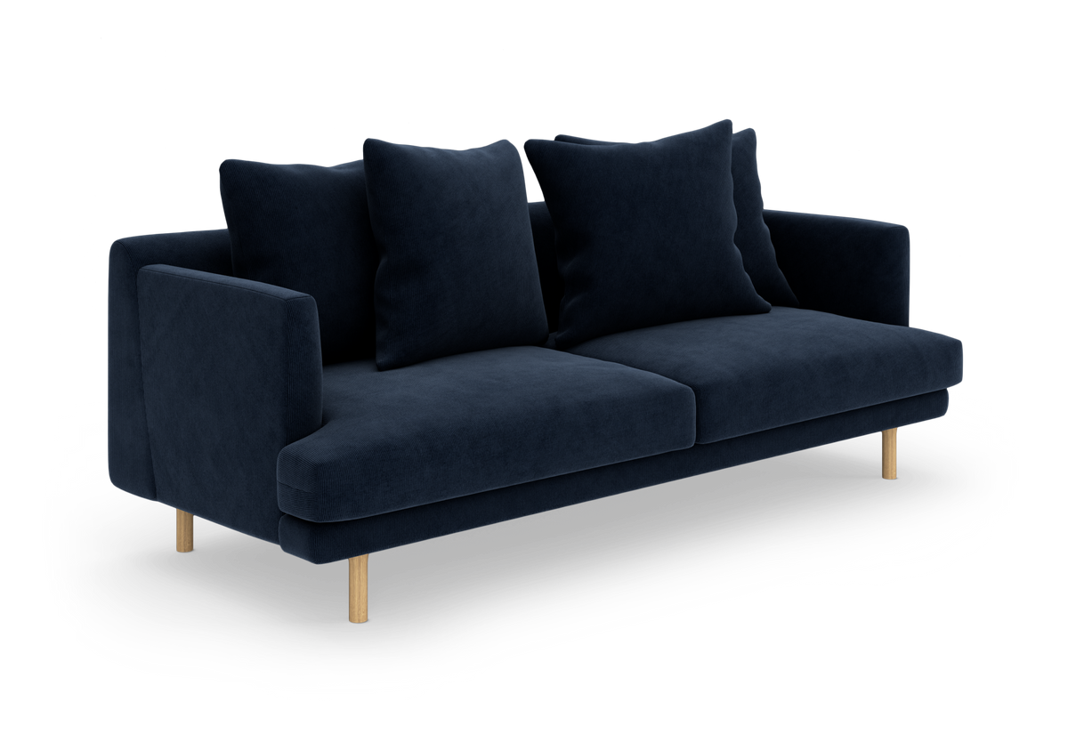 Mørkeblå tresæders sofa med store løse ryghynder og lyse træben, fotograferet i trekvart vinkel på hvid baggrund.