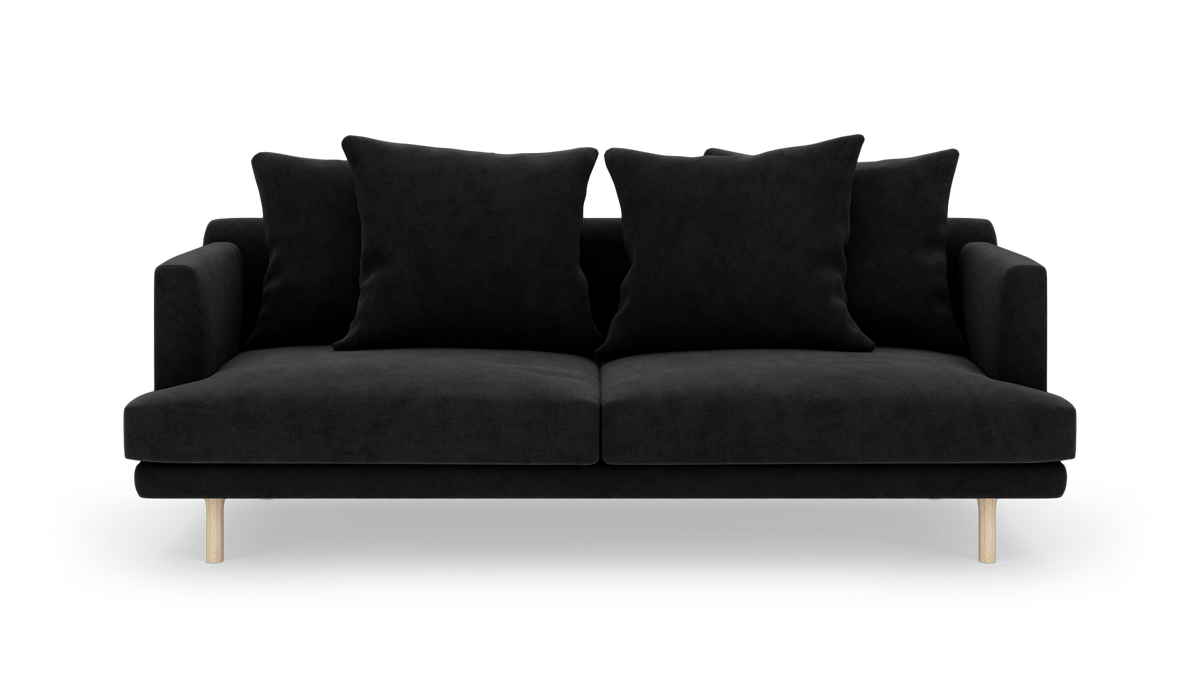 Sort sofa med fire store puder og lyse træben, isoleret mod hvid baggrund.