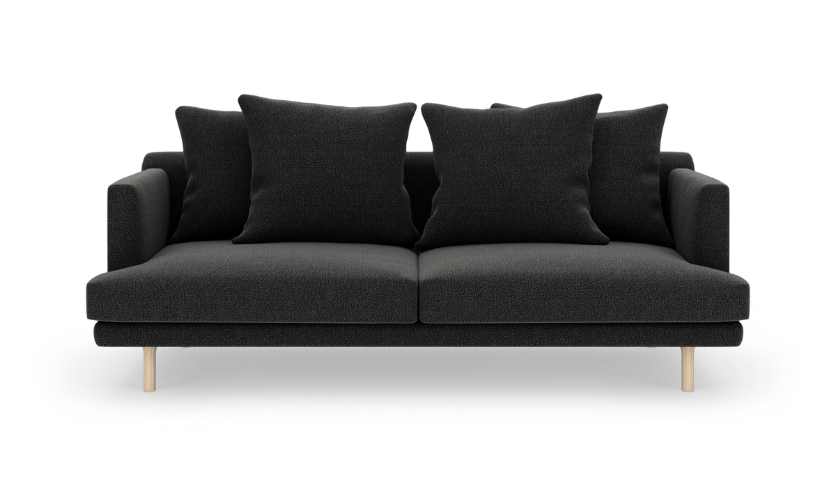 Sofa i mørkegråt stof med fire store puder og lyse træben, frilagt på hvid baggrund.