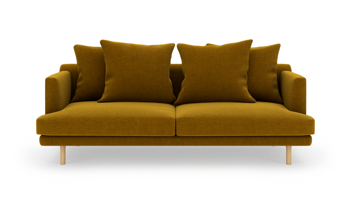 Sofa i sennepsgult stof med fire store puder, frilagt på hvid baggrund.