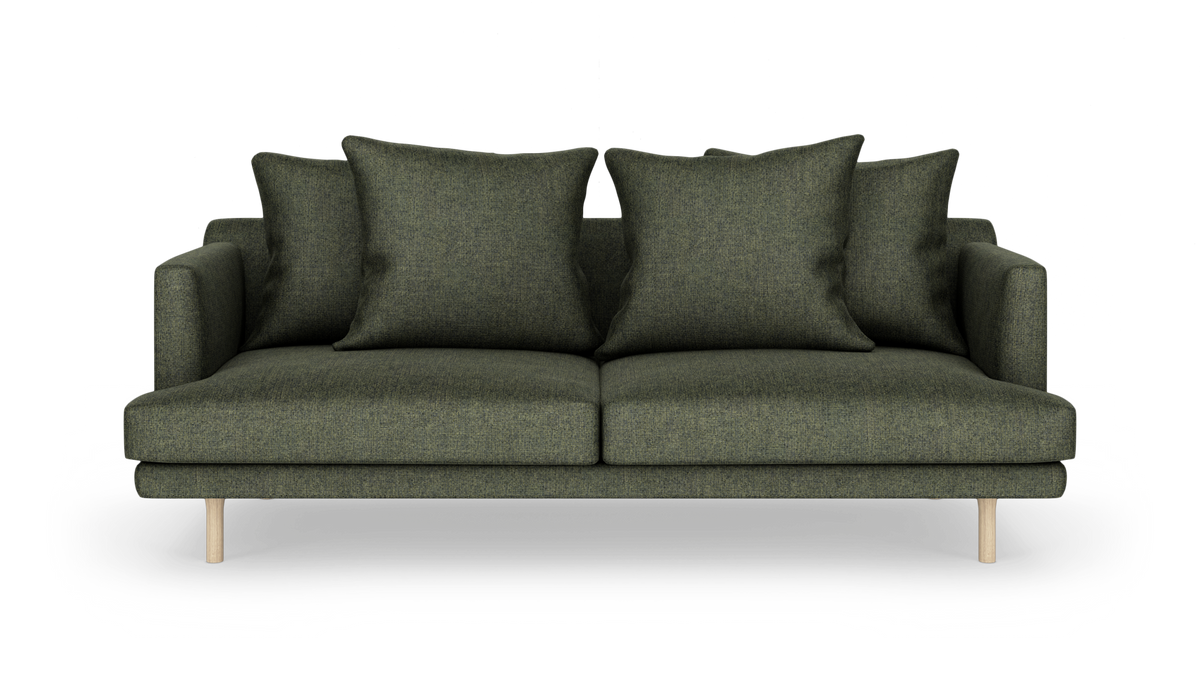 Mørkegrøn stofsofa med fire store puder og lyse træben, set forfra mod hvid baggrund.