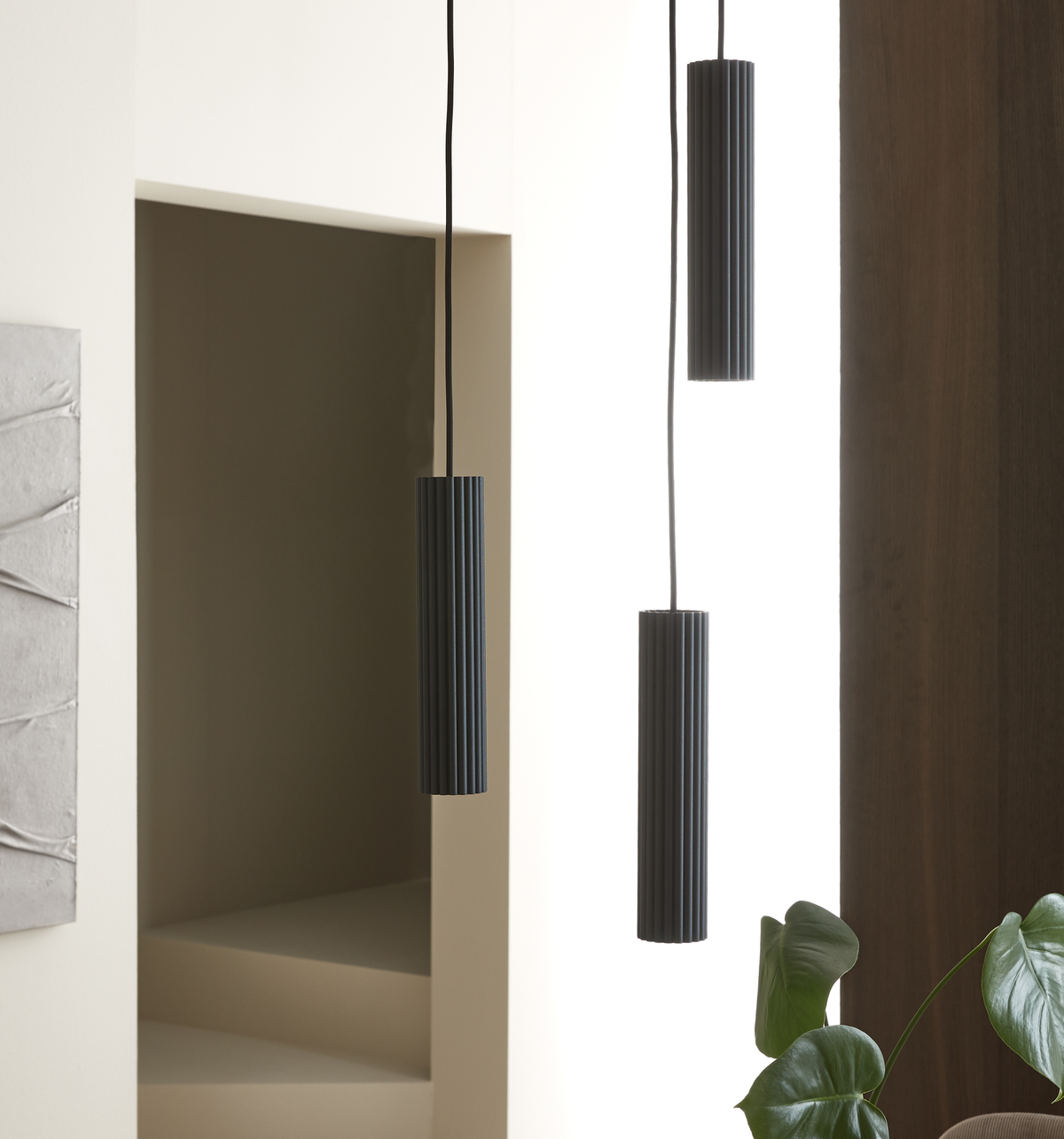 Tre sorte riflede pendler i et lyst, moderne rum med grønne blade og træpanel.