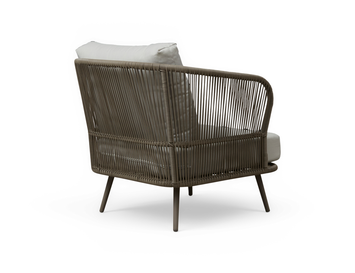 Lounge lænestol i flet med taupe stel og lyse puder, fotograferet skråt bagfra.