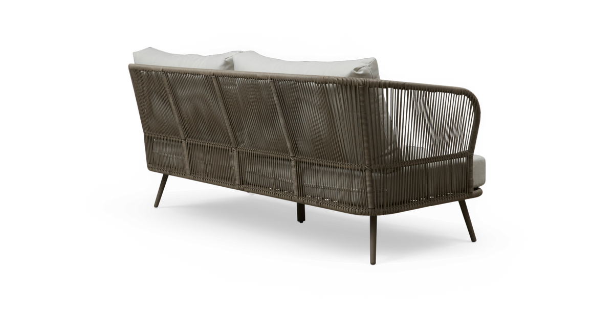 Bagfra skrå visning af en taupe rebflettet udendørs sofa med slanke ben og hvide puder, fritlagt.