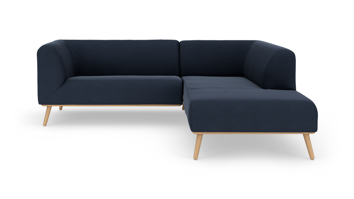 Mørkeblå L‑sofa med træben, fritlagt på hvid baggrund.