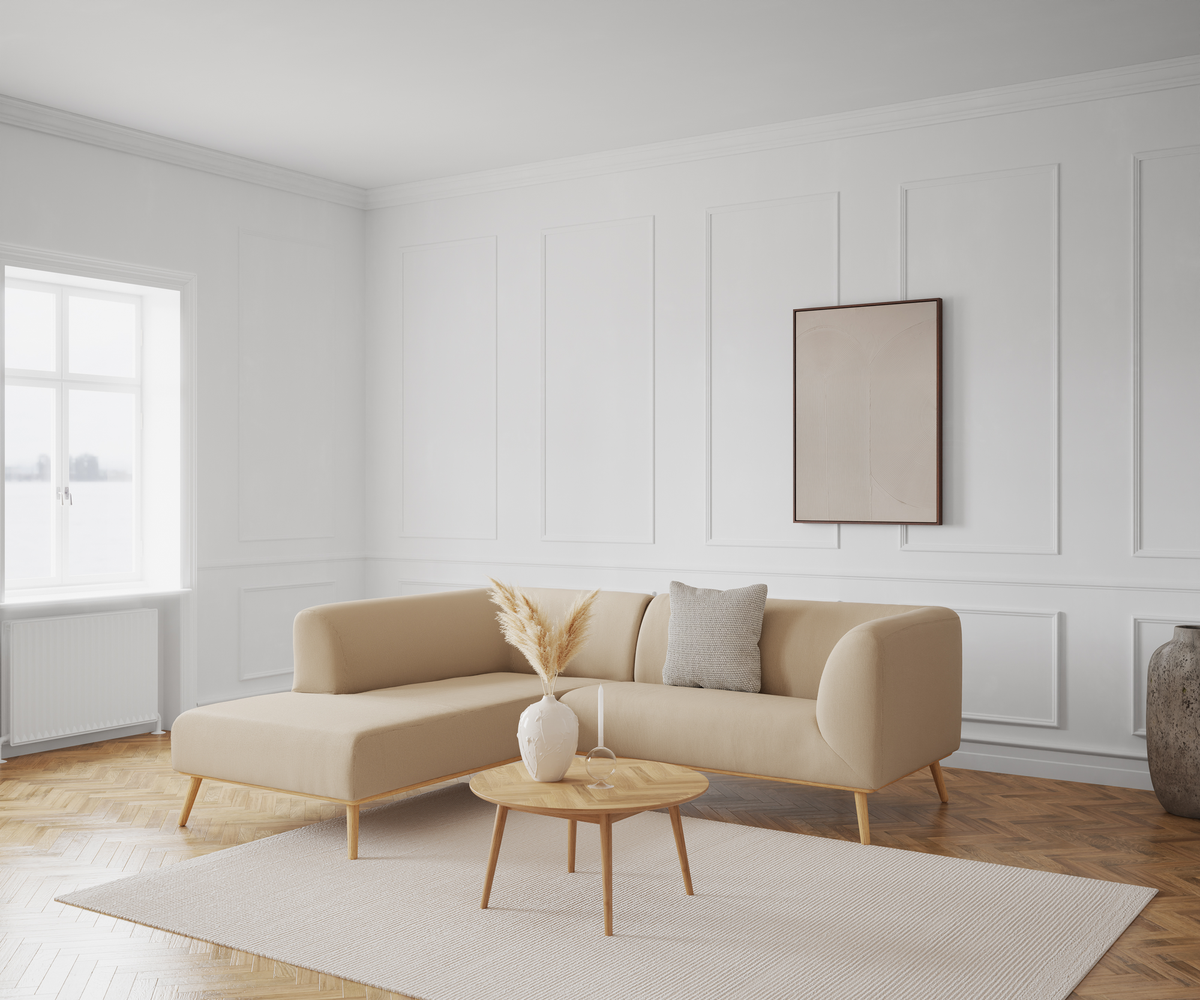 Beige hjørnesofa i minimalistisk stue med lyst sofabord, vase med pampas og hvide vægpaneler.