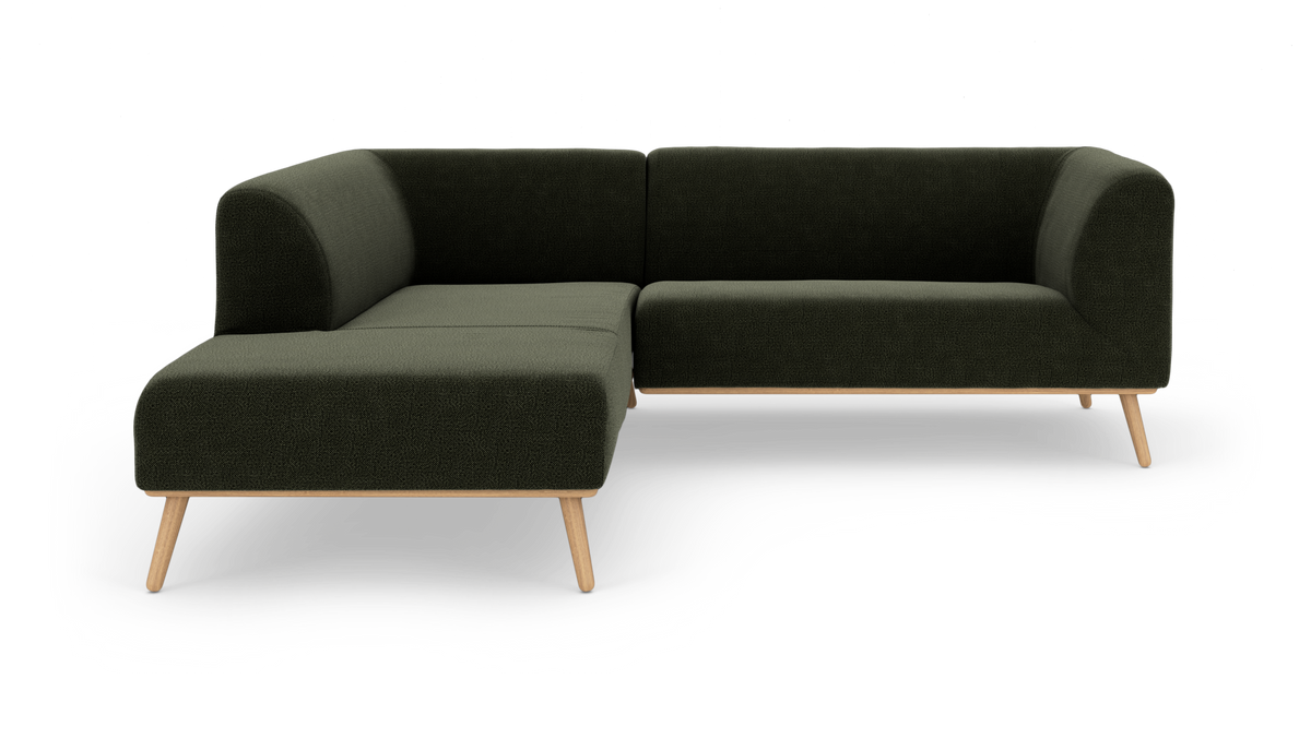 Mørkegrøn L-sofa i tekstil med lyse træben, frilagt på hvid studiobaggrund.