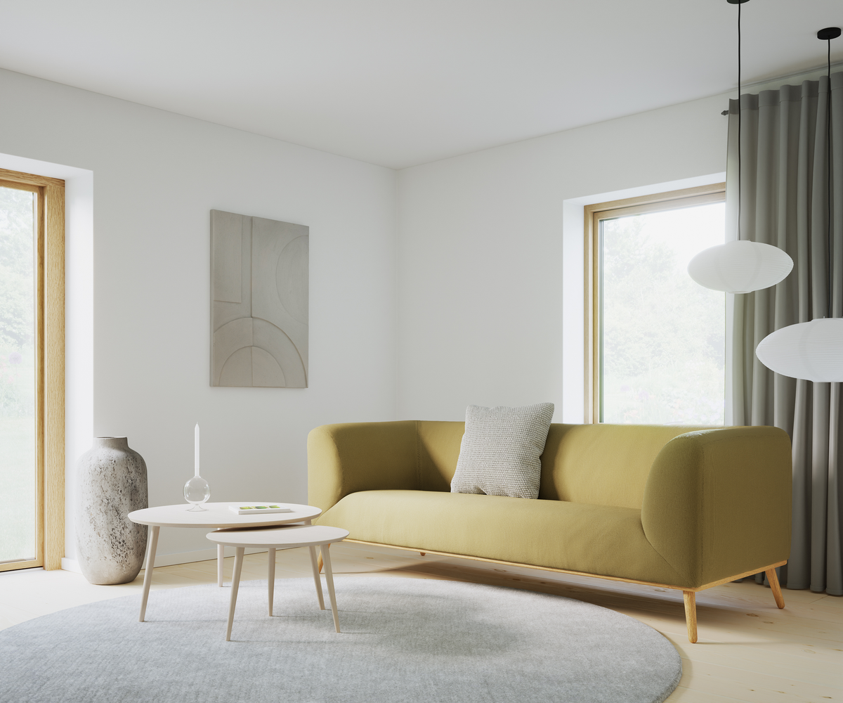 Lys skandinavisk stue med olivengrøn sofa, grå pude, to runde sofaborde med lys og bog, stor grå rund måtte, hængende rislamper, gardiner, vægkunst og store vinduer i dagslys.