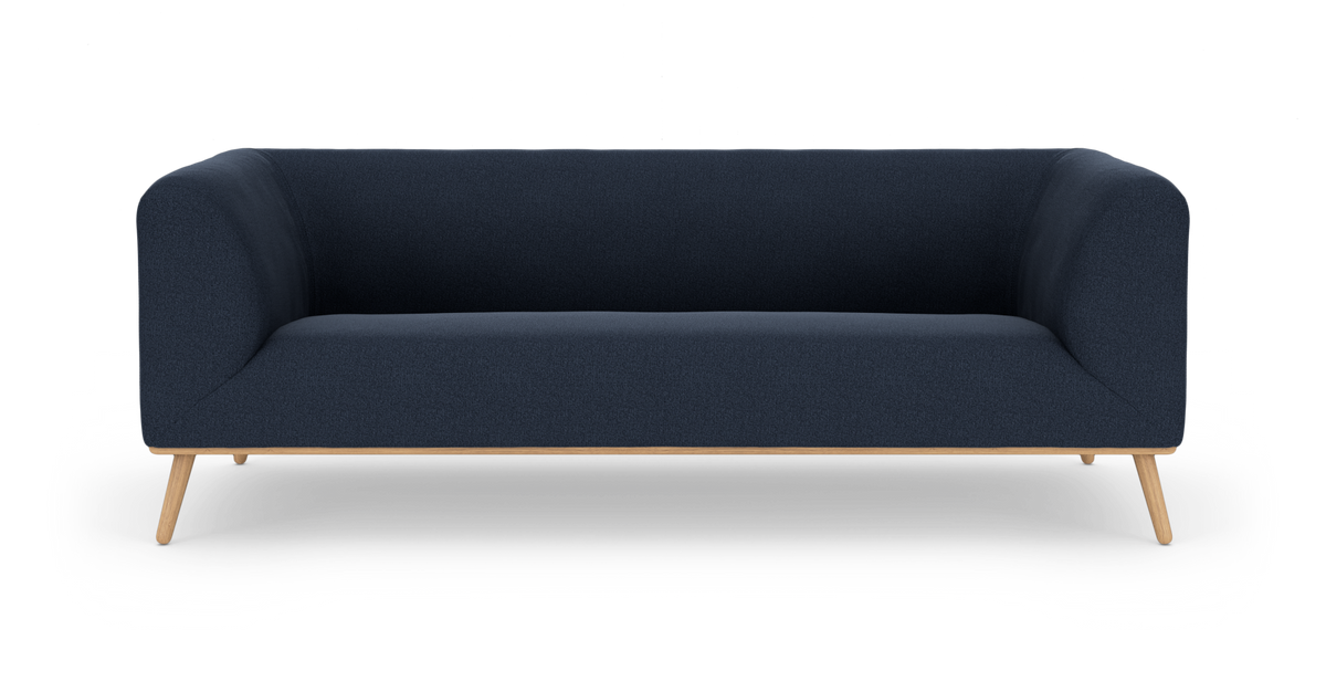 Mørkeblå, moderne tresæders sofa med afrundede armlæn og lyse egetræsben, frilagt på hvid baggrund.