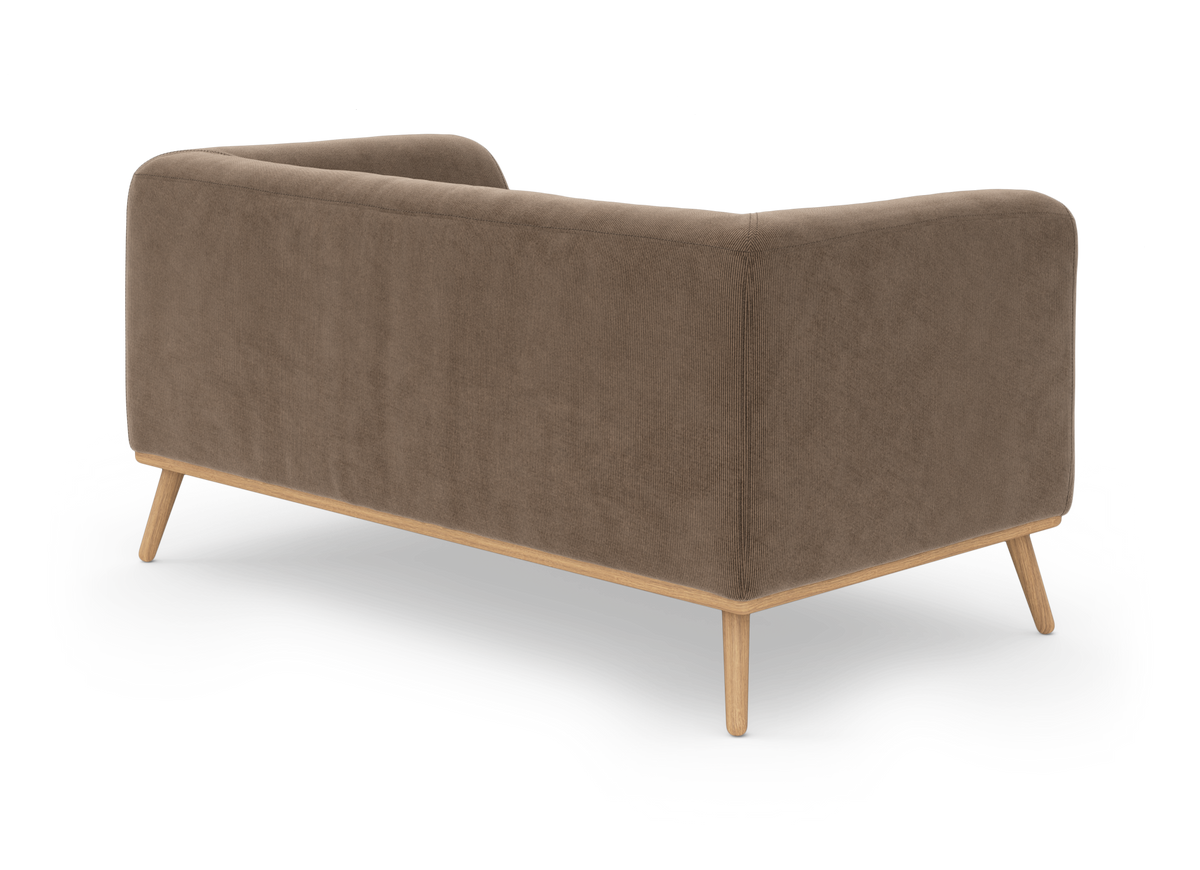 Brun sofa i kordfløjslignende stof med lyse træben, set bagfra i trekvart vinkel.