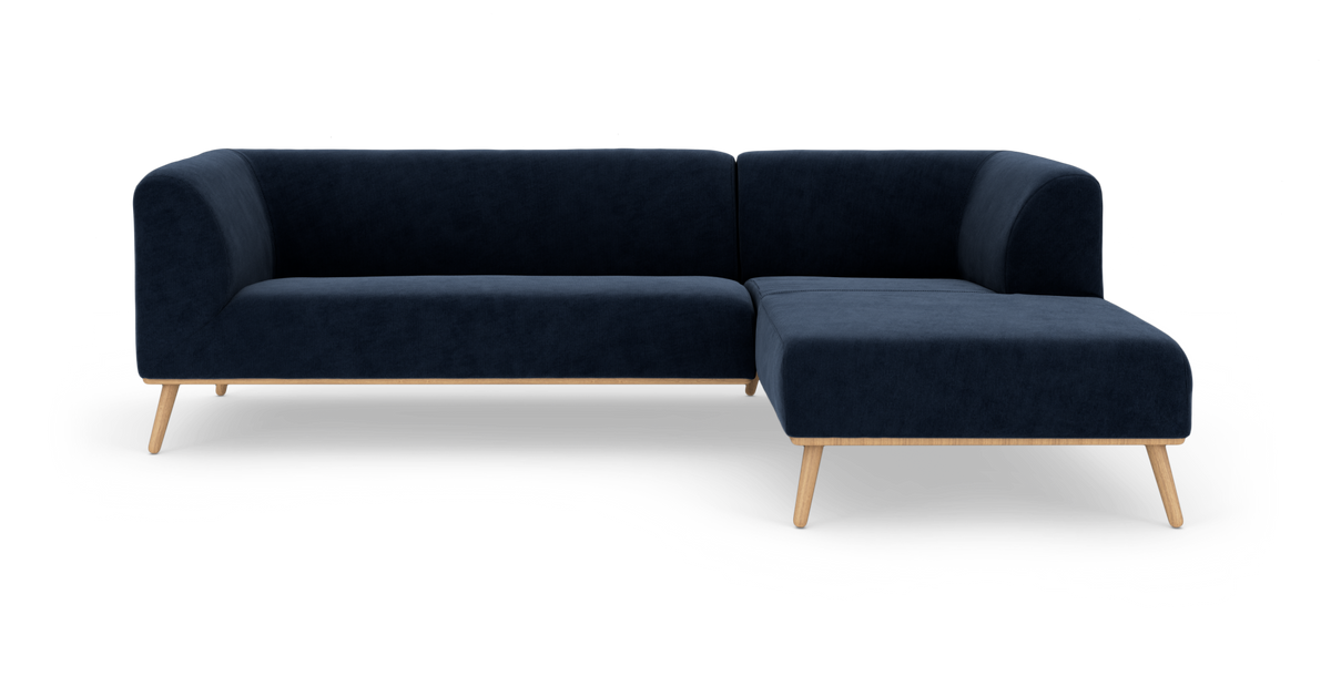 Mørkeblå modul-hjørnesofa med chaiselong og lyse træben, frilagt på hvid baggrund.