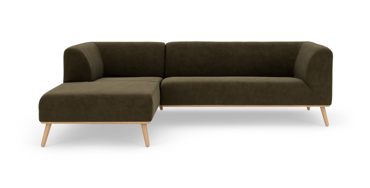 Mørkegrøn L‑sofa med venstrevendt chaiselong, polstret stof og lyse træben, frilagt på hvid baggrund.