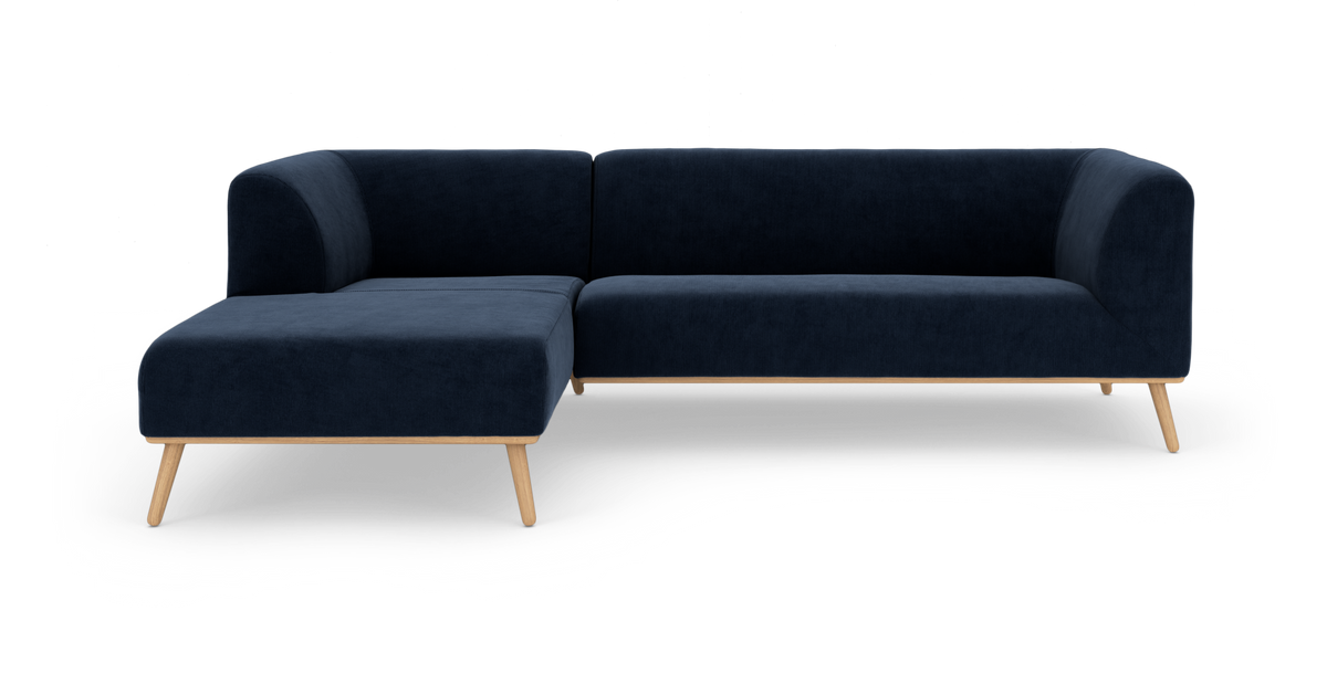 Mørkeblå hjørnesofa med chaiselong til venstre og lyse træben, frilagt på hvid baggrund.
