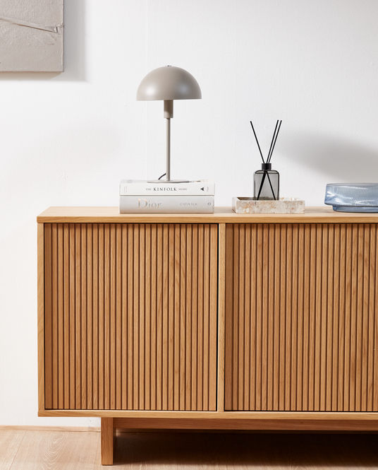 Ribbet egetræsskab med beige kuppelformet bordlampe på bøgerne ”The Kinfolk Home” og ”Dior Catwalk” samt duftpinde på en lille bakke.