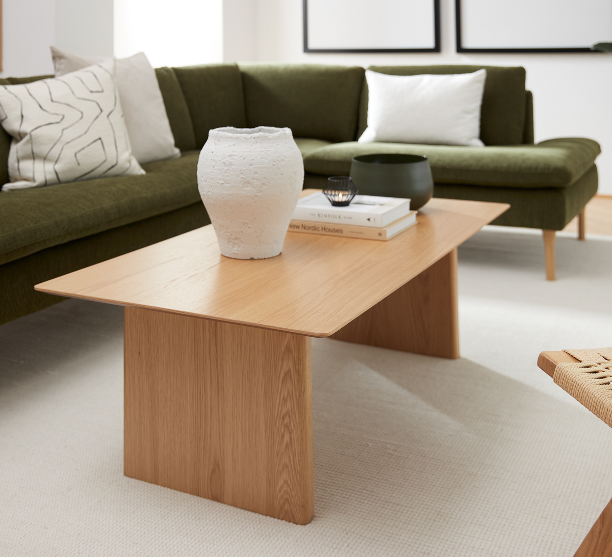 Stue med olivengrøn sofa og lyst egetræsbord med hvid vase, bøgerne “New Nordic Houses” og “Kinfolk”, samt en skål ovenpå.