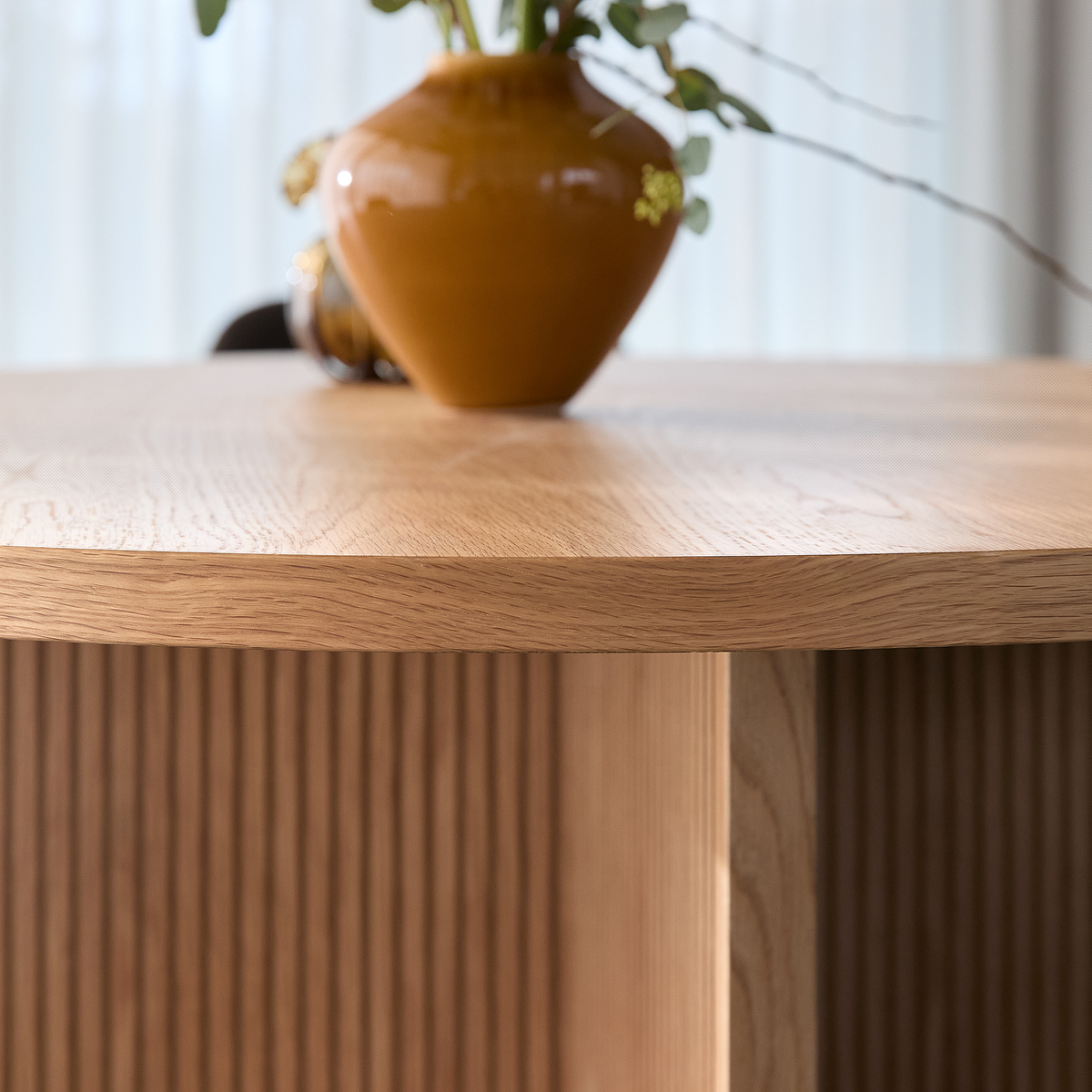 Nærbillede af rund bordplade i lys eg med brun glaseret vase og eucalyptus i et lyst indendørsmiljø.