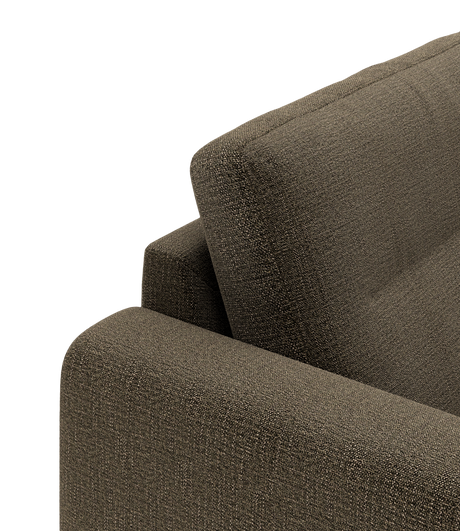 Nærbillede af brun stofsofa med armlæn og ryglæn set i hjørnevisning mod mørk baggrund.