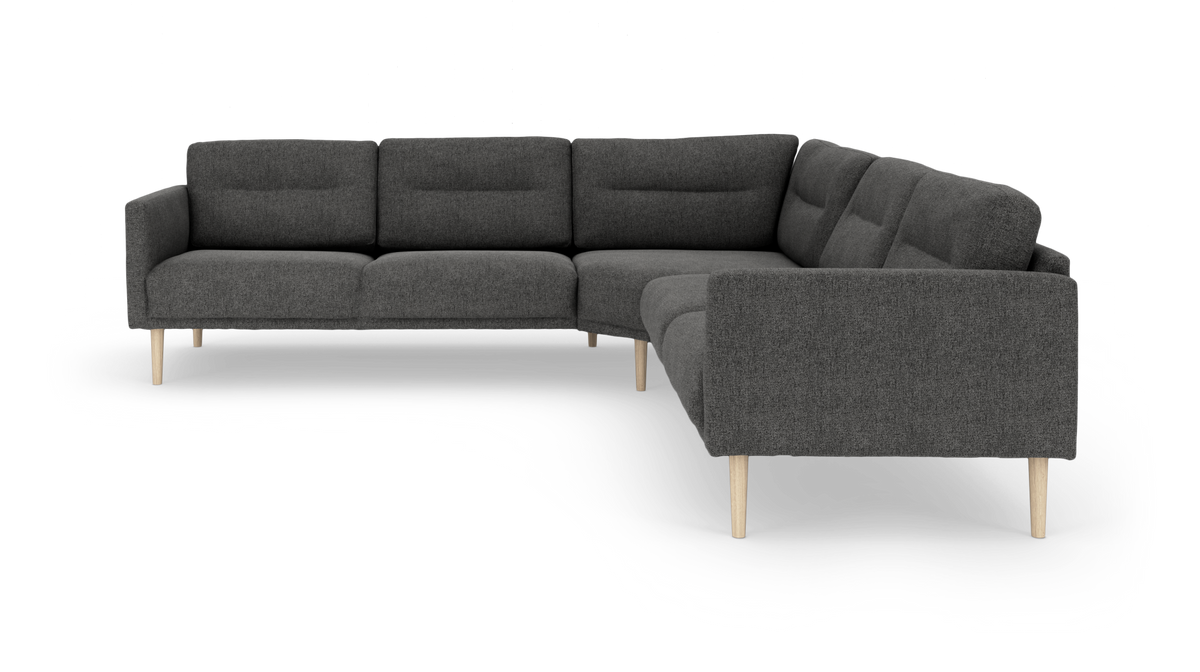 Mørkegrå hjørnesofa i stof med lyse træben, fotograferet skråt forfra på hvid baggrund.