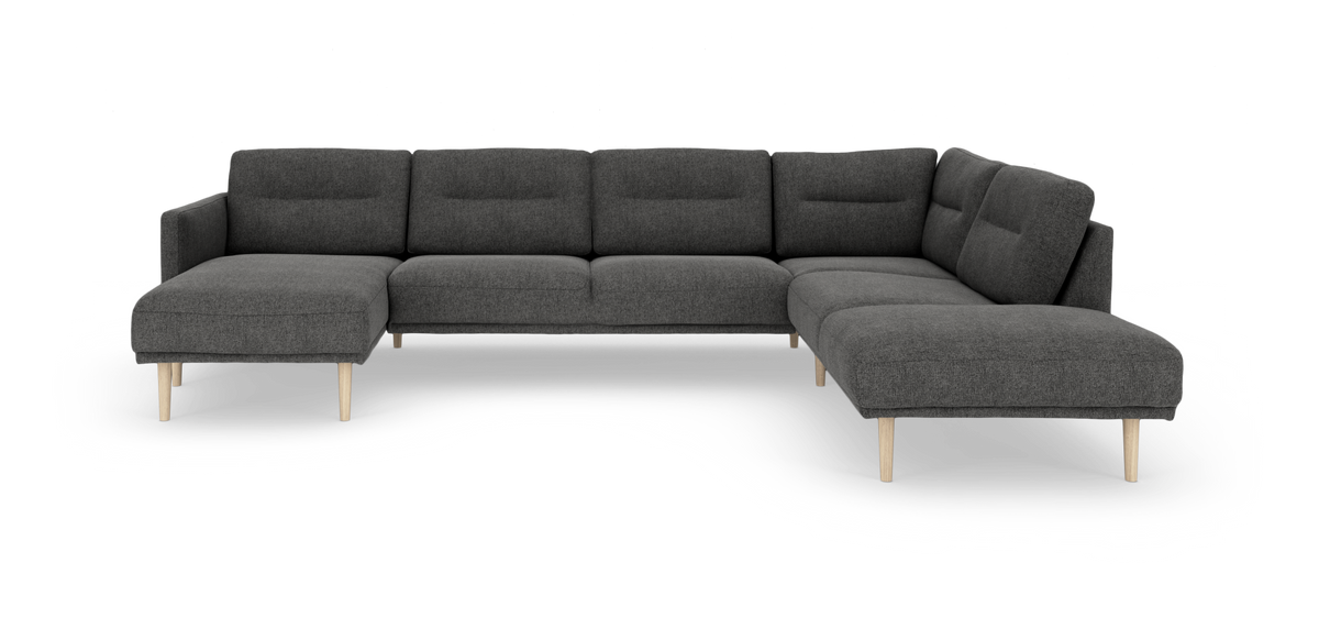 Mørkegrå modulsofa i U‑form med chaiselong i begge ender og lyse træben, frilagt på hvid baggrund.