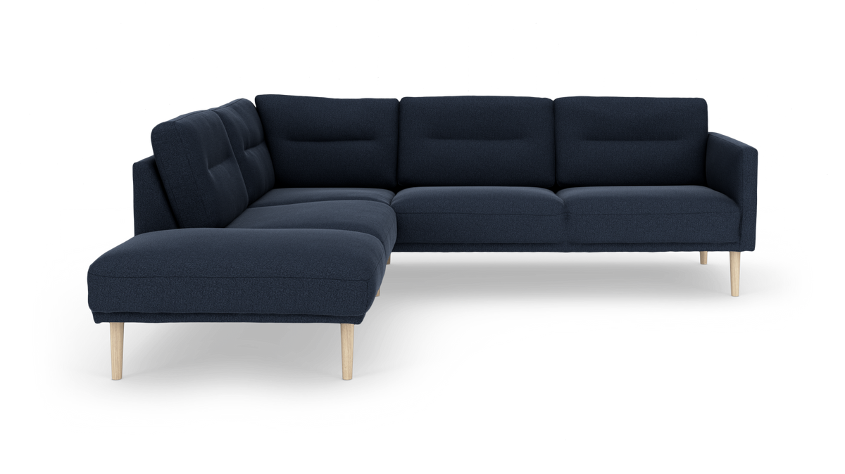 Mørkeblå hjørnesofa med chaiselong til venstre og lyse træben, frilagt på hvid baggrund.