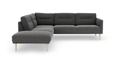 Mørkegrå L‑sofa med chaiselong og lyse træben, i studiemiljø.