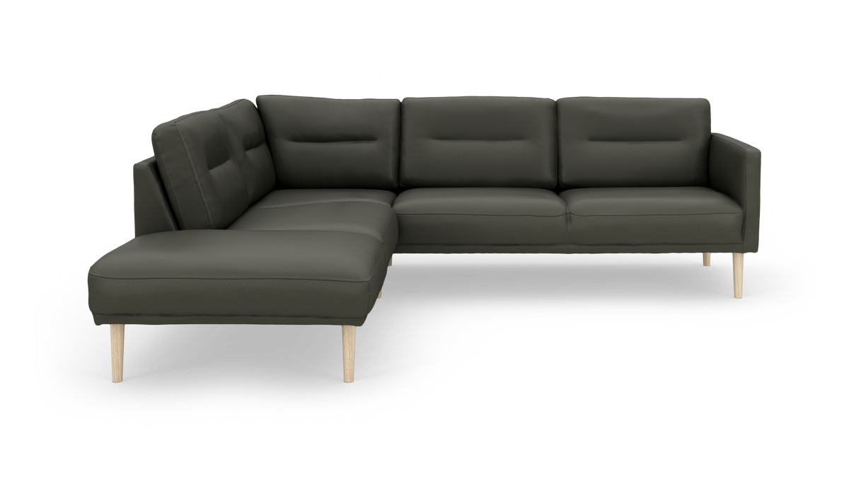 Mørkegrøn L-sofa med chaiselong til venstre og lyse træben, frilagt på hvid baggrund.