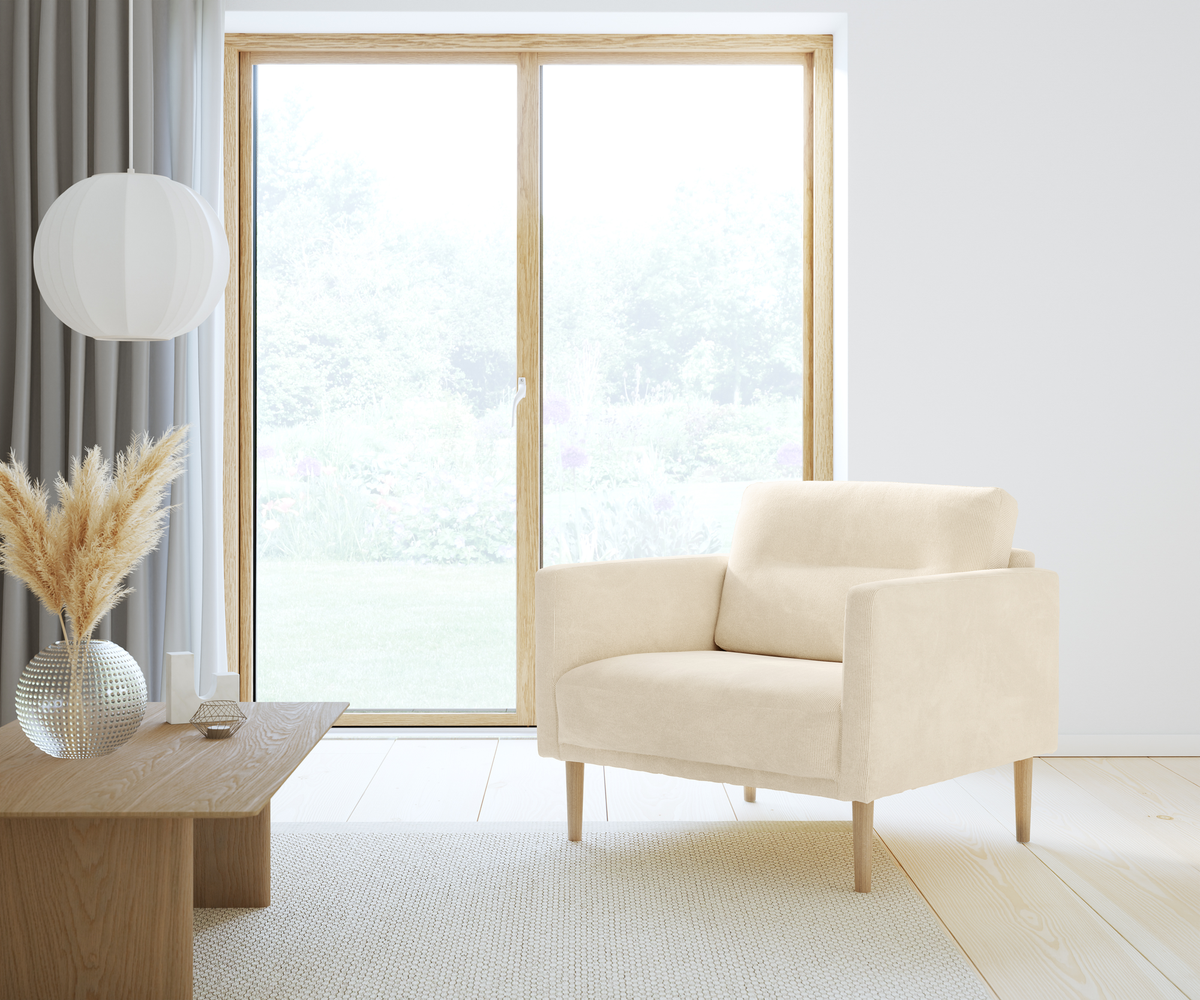 Lyst skandinavisk stue med beige lænestol, træbord med vase med pampasgræs og rund hvid pendel ved stort vindue i dagslys.