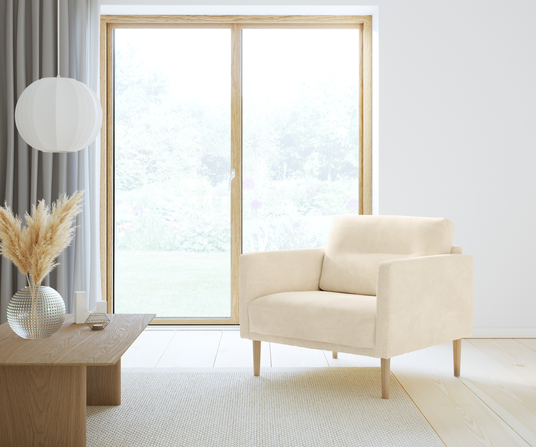 Lyst skandinavisk stue med beige lænestol, træbord med vase med pampasgræs og rund hvid pendel ved stort vindue i dagslys.